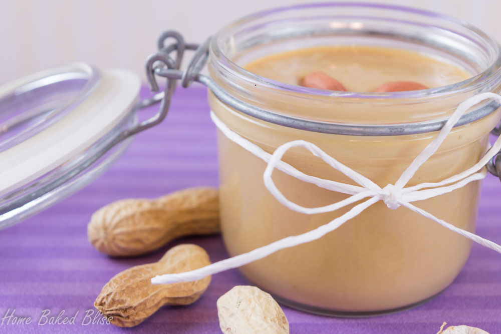 A jar of peanut butter on a purple background next to shelled peanuts.