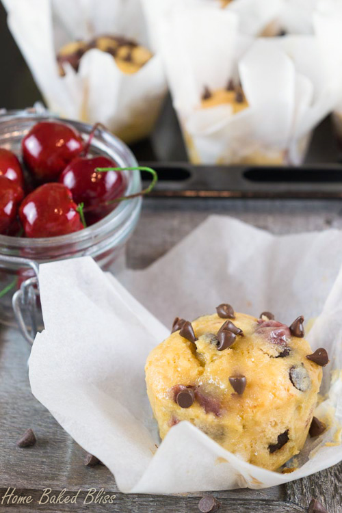 Cherry chocolate chip muffin in a parchment paper liner beside a jar of cherries.