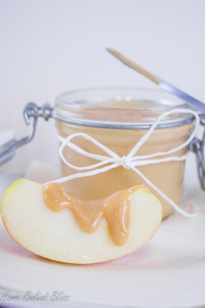 A jar of homemade peanut butter next to an apple slice drizzled with peanut butter.
