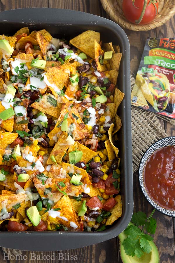 Loaded nachos drizzled with a sour cream sauce alongside a dish of salsa.