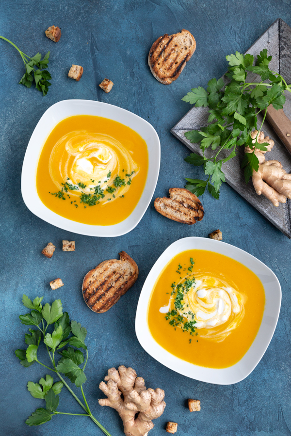 Two bowls of creamy vegan carrot coconut soup on a blue background