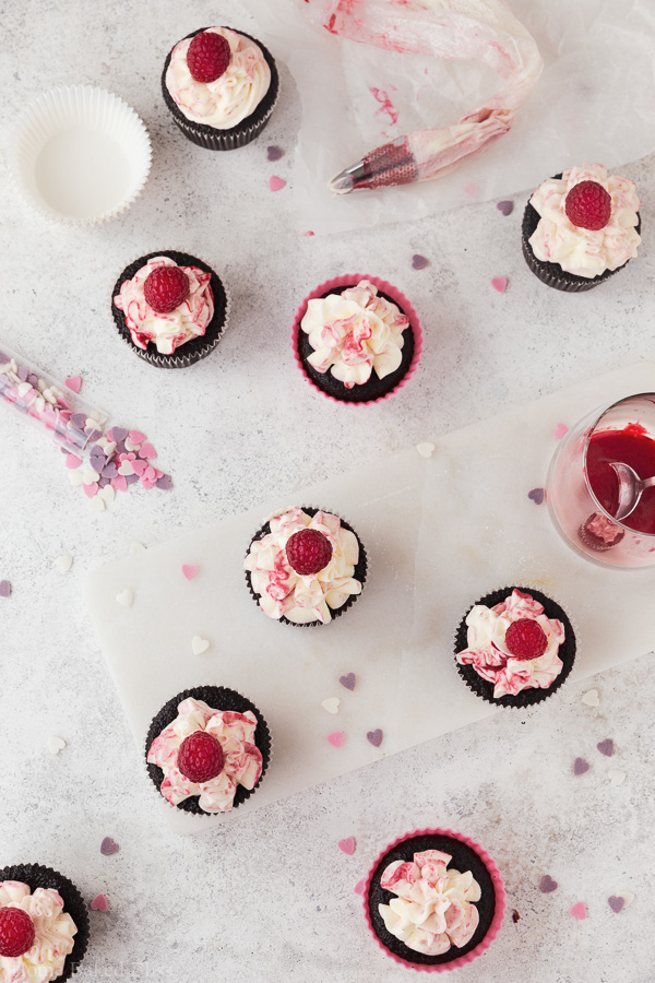 Chocolate cupcakes decorated with fresh raspberries on white background with pink sprinkles