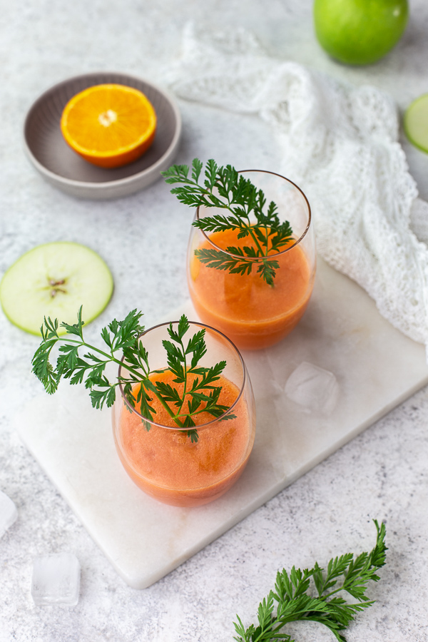 Two glasses of carrot apple smoothie on a white marble tray