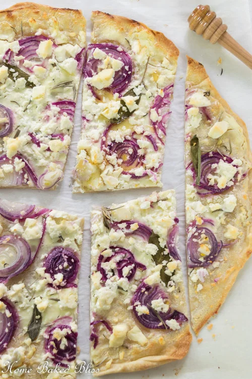 Tarte Flambée with onions and feta on parchment paper sliced into pieces.