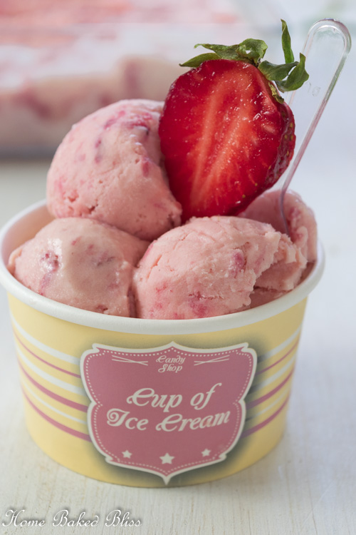 Three scoops of strawberry ice cream in a paper cup garnished with a strawberry slice