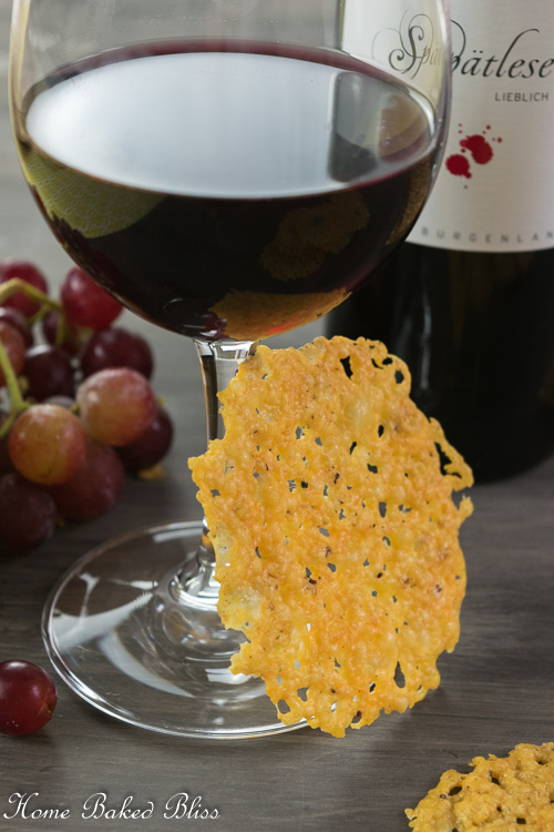 A crispy cheese cracker leaning against a glass of red wine