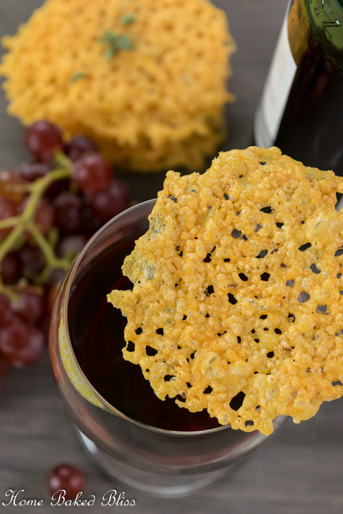A crispy cheese cracker sitting on top of a glass of red wine.