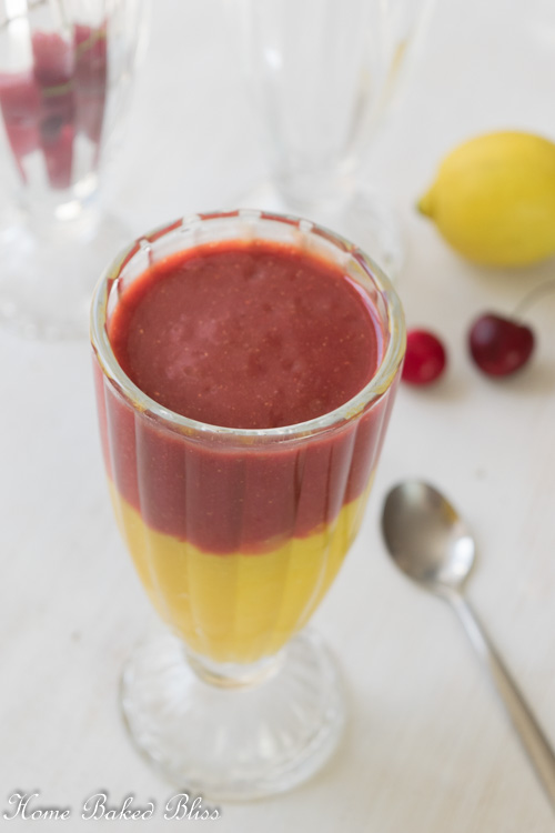 A vibrant Mango Cherry Smoothie in a tall glass next to a long spoon