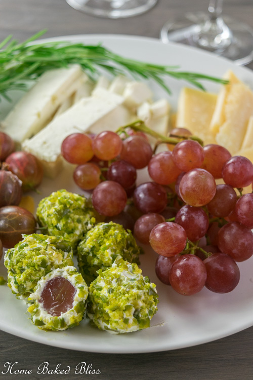 Cream Cheese and Pistachio Bites on a plate alongside grapes, cheese and herbs.