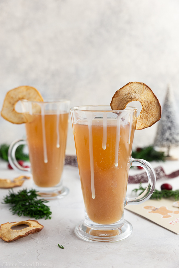 Apple cider in glasses garnished with sweetened condensed milk and dried apple slices.