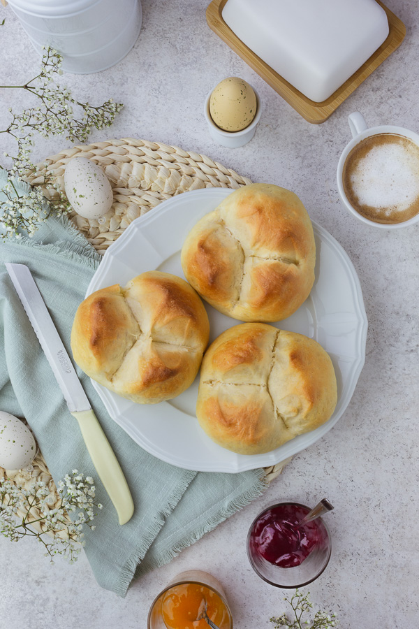 Three vegan easter breads on a white plate next to a cup of coffee