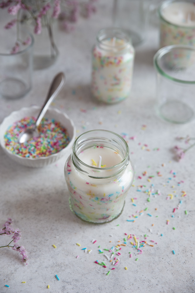A DIY sprinkle candle next to a bowl of sprinkles