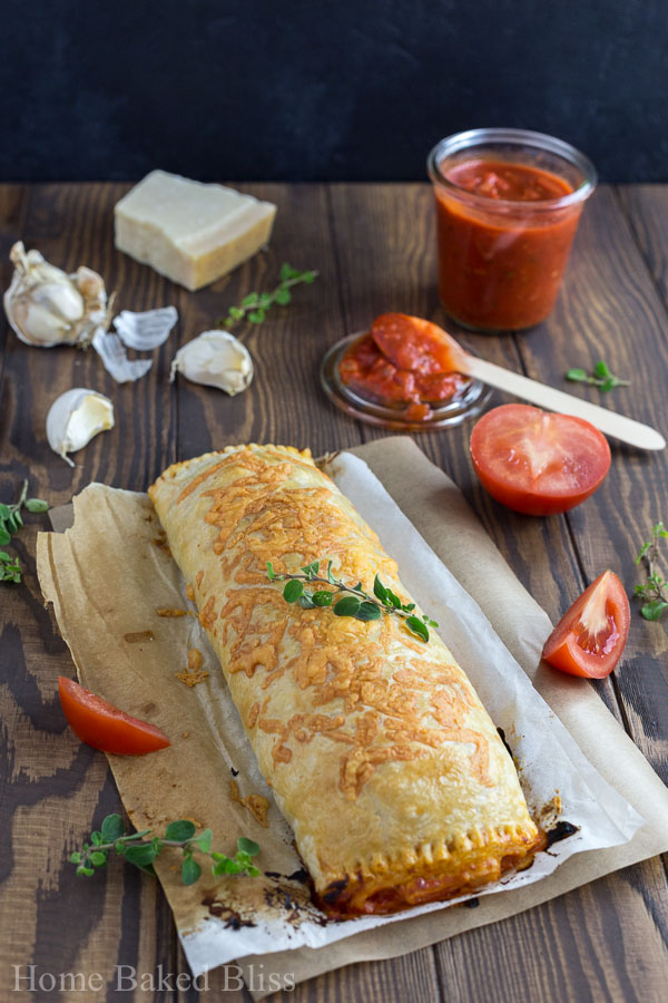 Cheesy calzone on parchment paper garnished with fresh oregano.
