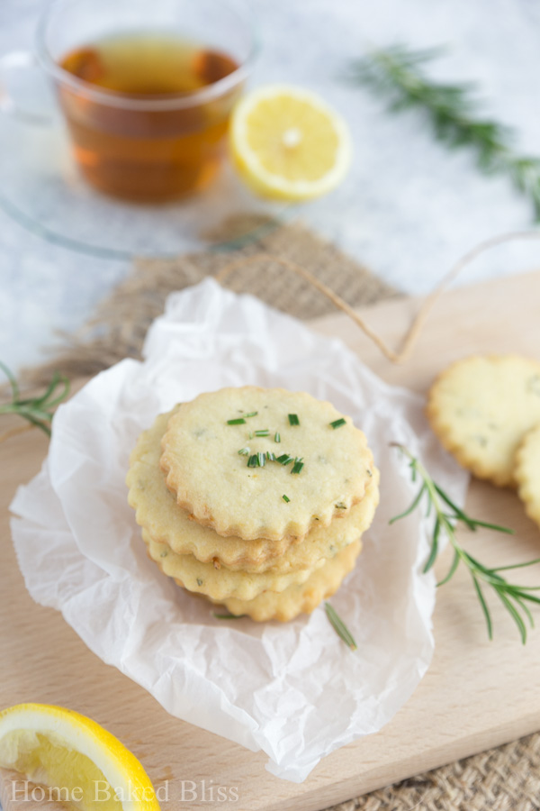 Rosemary lemon cookies sitting on a cutting board in front of a cup of tea