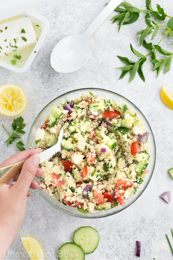 A hand mixing the couscous salad with a large spoon.