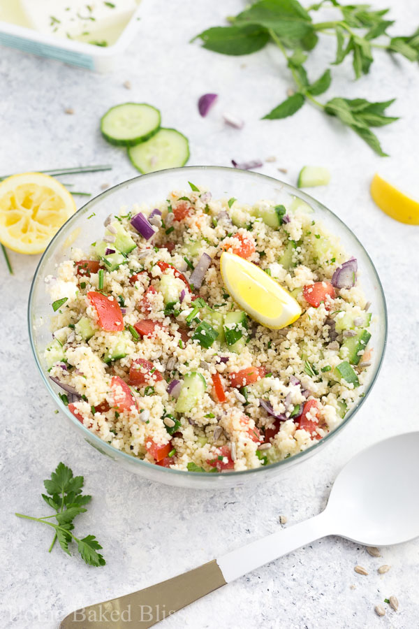 A colourful couscous salad with cucumber, tomatoes, feta cheese and onions in a glass bowl.