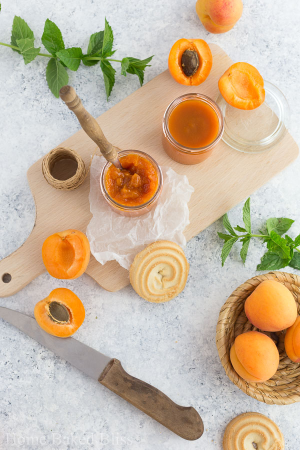 Two jars of homemade apricot jam on a wooden board.