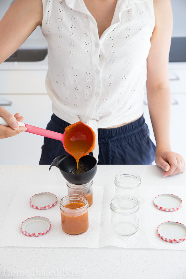 Pouring the apricot jam into sterilized glass jars with a funnel.