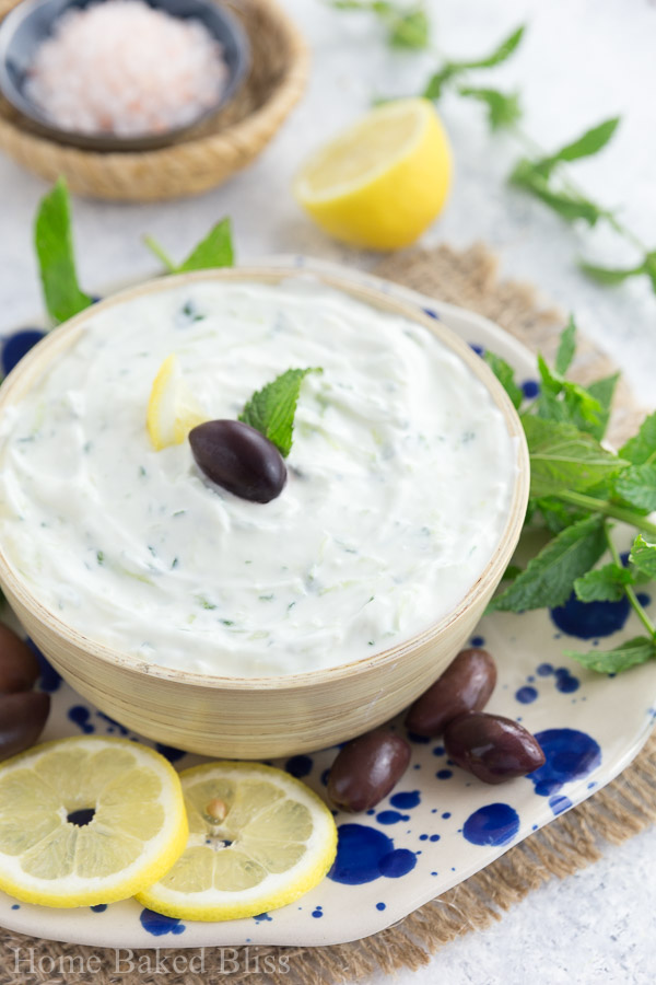 Greek tzatziki in a wooden bowl garnished with an olive and lemon.