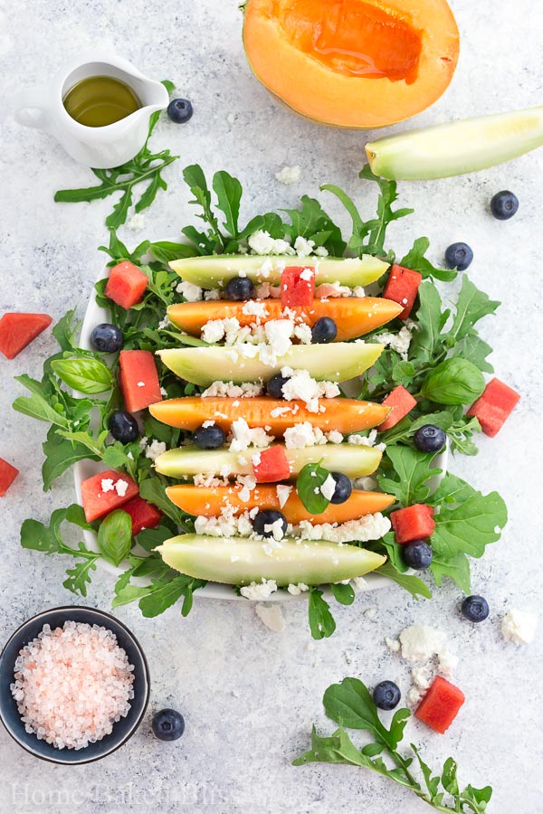 A melon salad with feta cheese, arugula, blueberries, watermelon on a white plate.