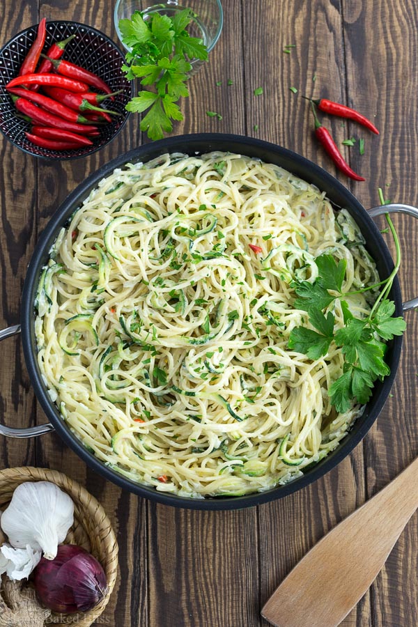 A pan with creamy zucchini noodles next to a bowl of red chilis.