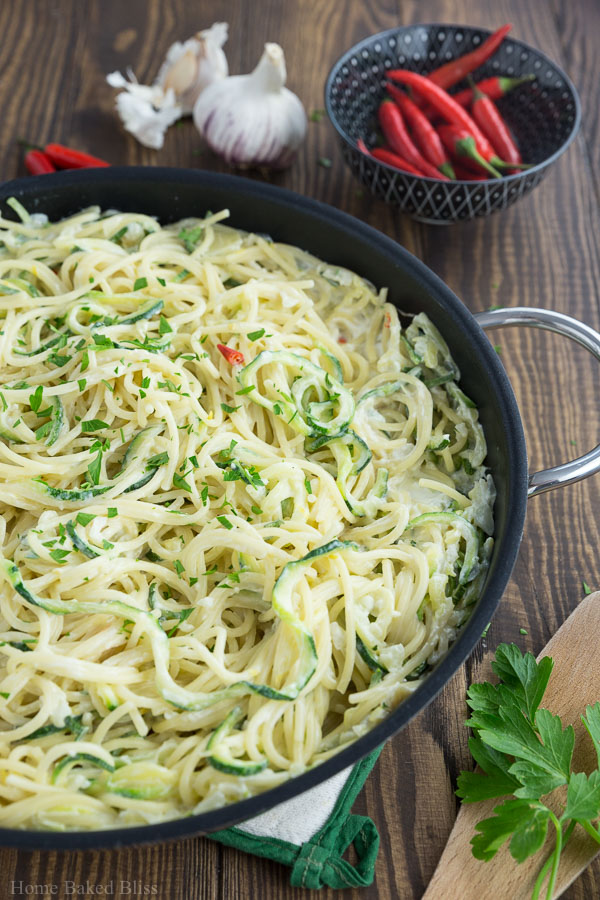 Creamy zucchini noodles in a black pan topped off with parsley.