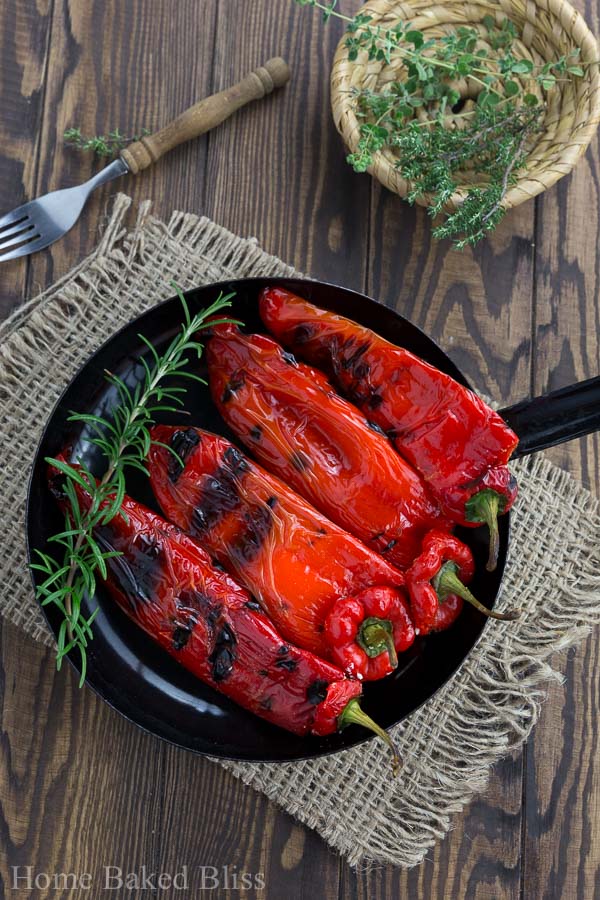 Grilled peppers with feta in a black pan next to to a bowl of herbs