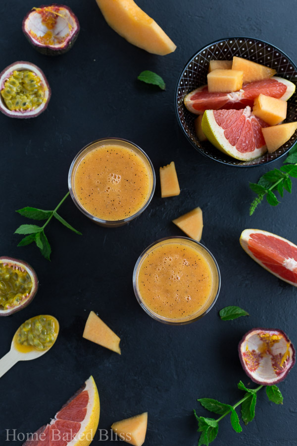 An overhead view of two glasses of tropical smoothie beside slices of grapefruit and melon