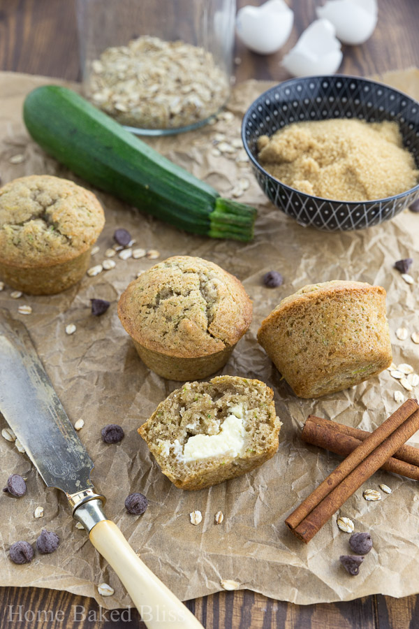 Zucchini muffins filled with cream cheese next to a butter knife and cinnamon sticks.