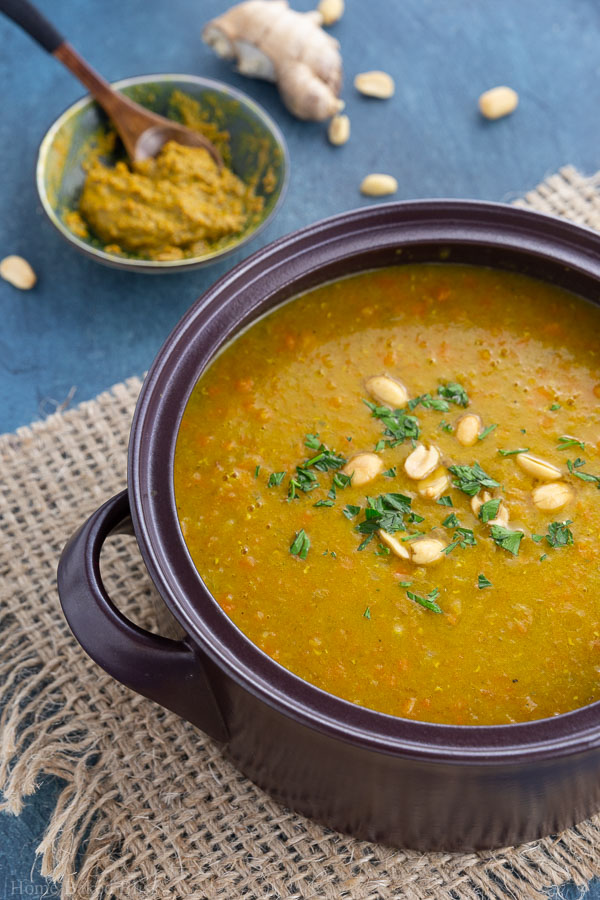A large pot of chunky carrot lentil curry soup garnished with parsley and peanuts.