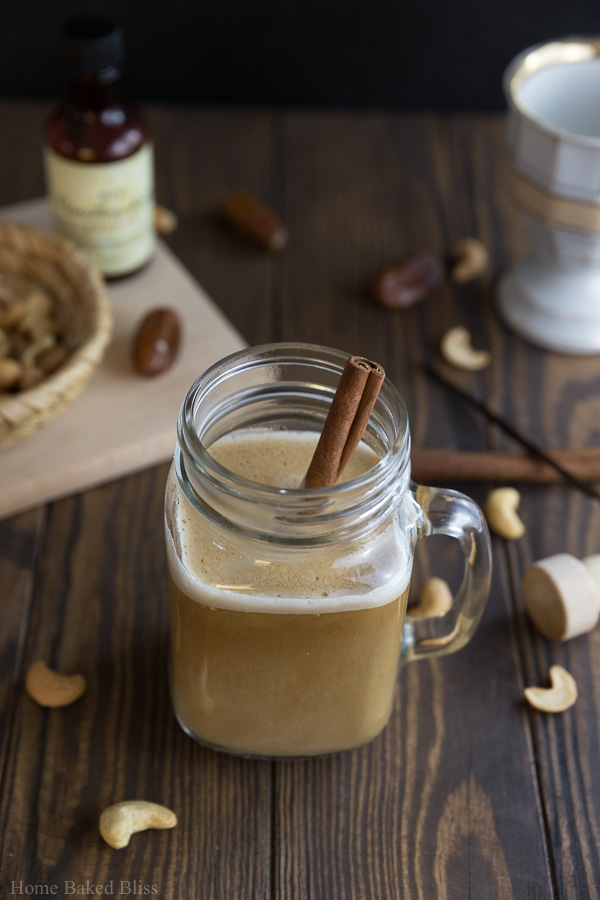 A mason jar glass filled with cashew cinnamon coffee and a cinnamon stick.