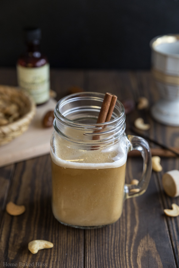 A mason jar glass filled with cashew cinnamon coffee and a cinnamon stick.