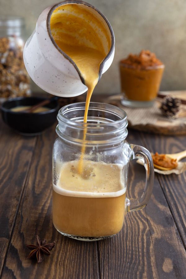 Pumpkin spice milk being poured over hot coffee.