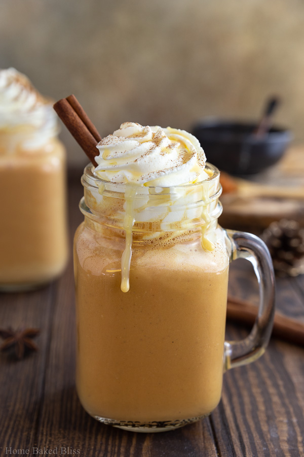 A pumpkin spice latte in a mason jar garnished with whipped cream and a cinnamon stick.