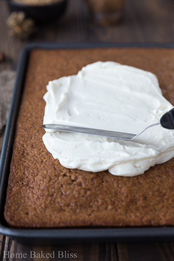 Frosting being spread onto a spice sheet cake with a spatula