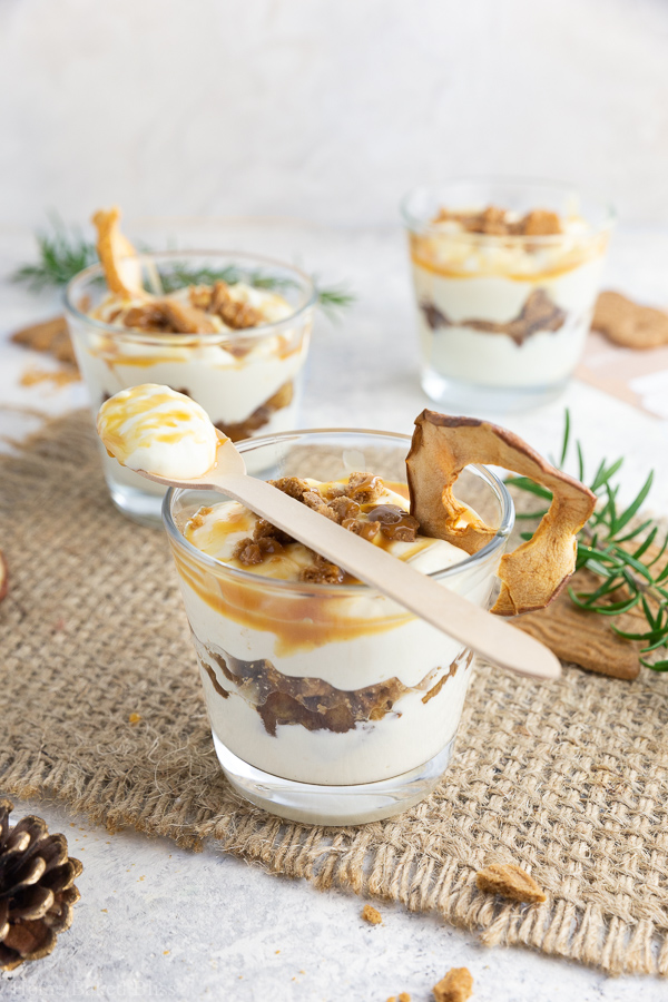 Speculoos tiramisu with cinnamon apples and caramel sauce in glasses with a wooden spoon on top.