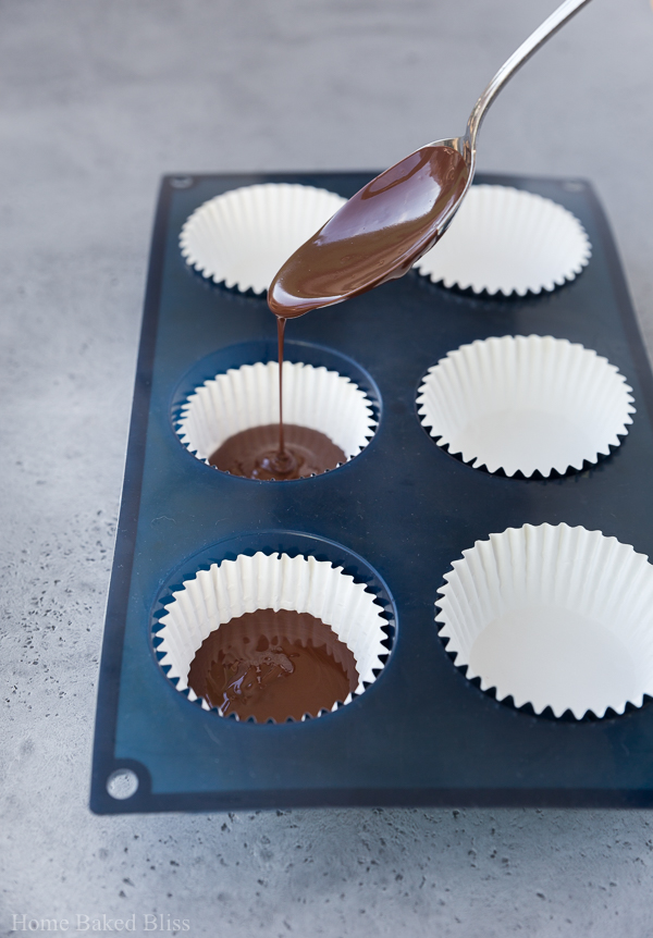 Pouring melted chocolate into cupcake liners with a tablespoon.