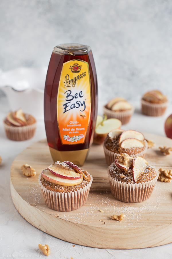 Apple walnut muffins on a round wooden board next to a tube of honey.