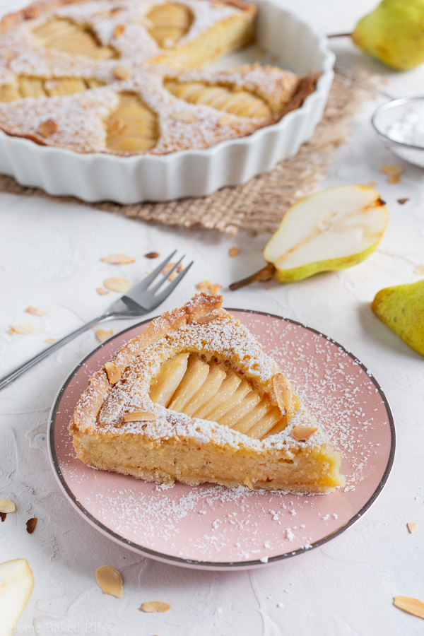 A slice of Pear Frangipane Tart sprinkled with powdered sugar and garnished with toasted sliced almonds on a pink plate