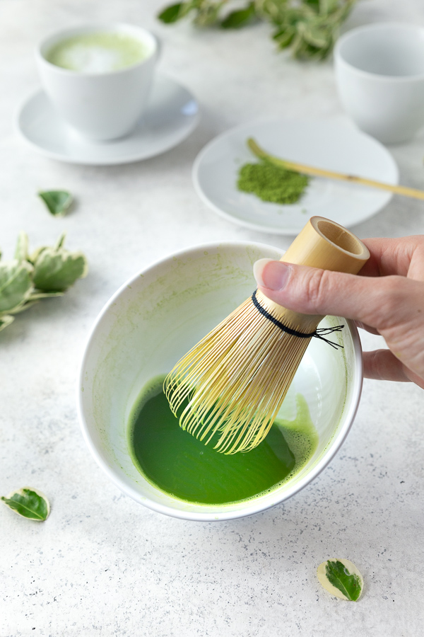 Frothing matcha tea in a white bowl with a bamboo brush