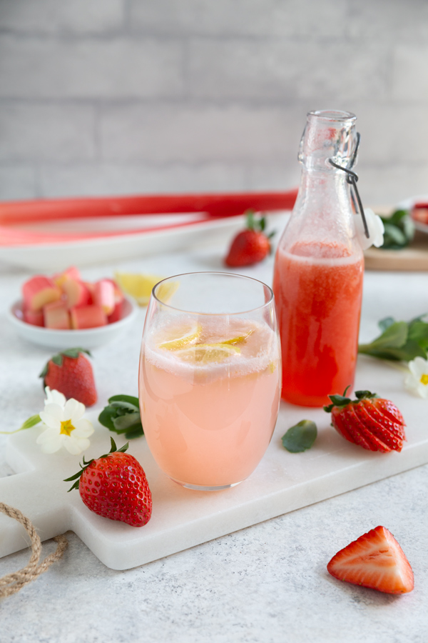 Eine kleine Flasche Erdbeer-Rhabarber-Sirup neben einem Glas Limonade