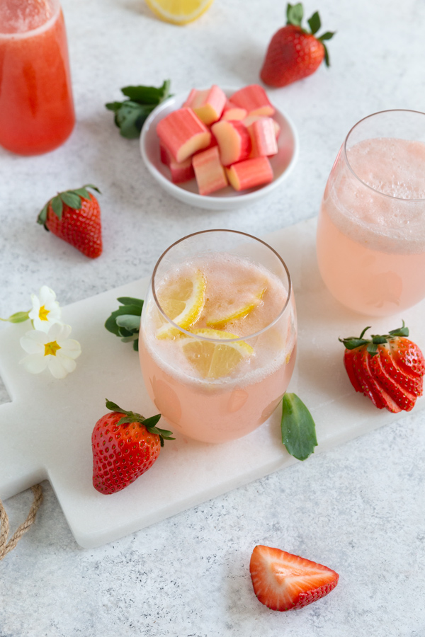 A glass of strawberry rhubarb lemonade garnished with fresh lemons