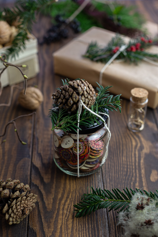 Buttons in a glass jar decorated with a pine cone and greenery
