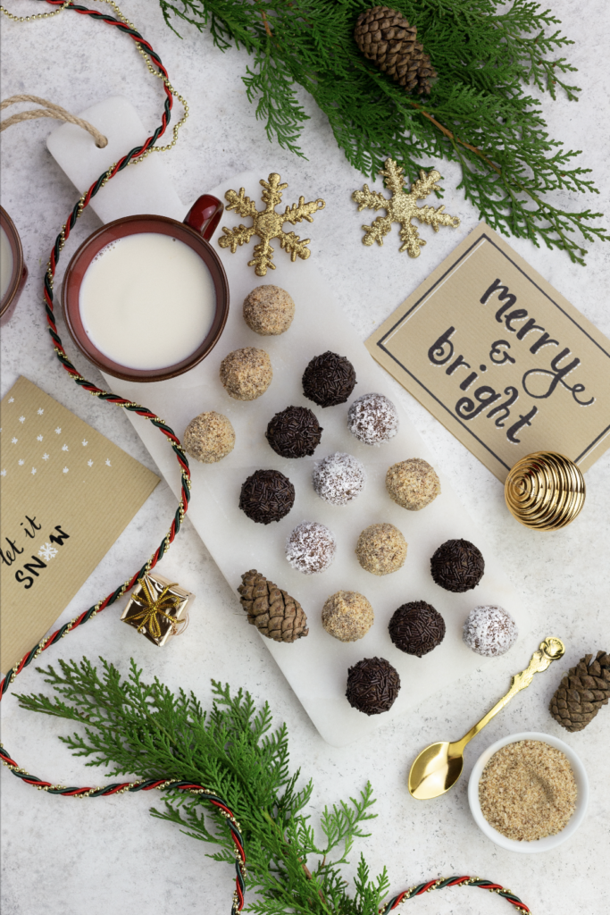 Vegan rum truffles on white plate next to a cup of milk and Christmas cards