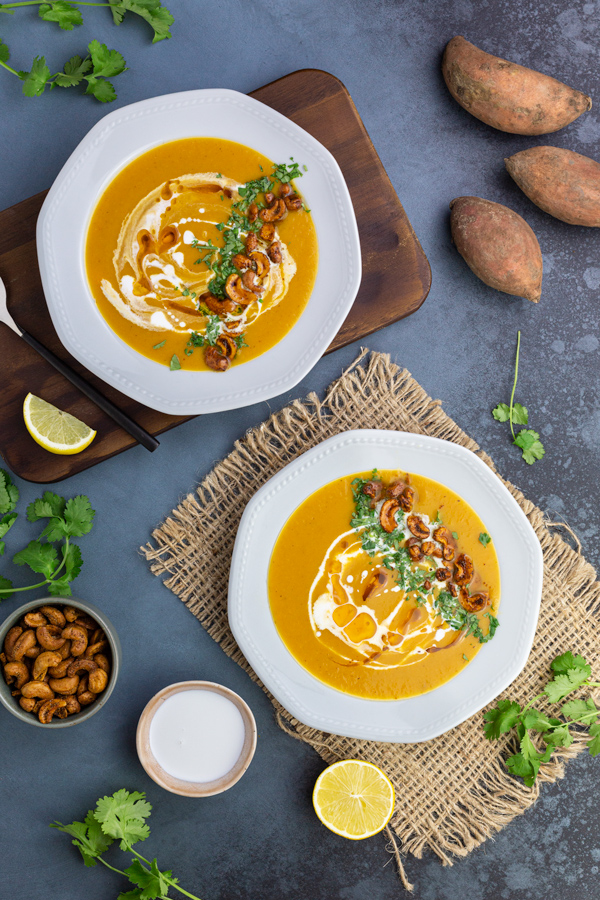 Two bowls of sweet potato and leek soup garnished with curried cashews, coriander, cream and oil