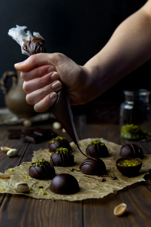 Piping chocolate decorations on vegan Miso Caramel & Pistachio Truffles