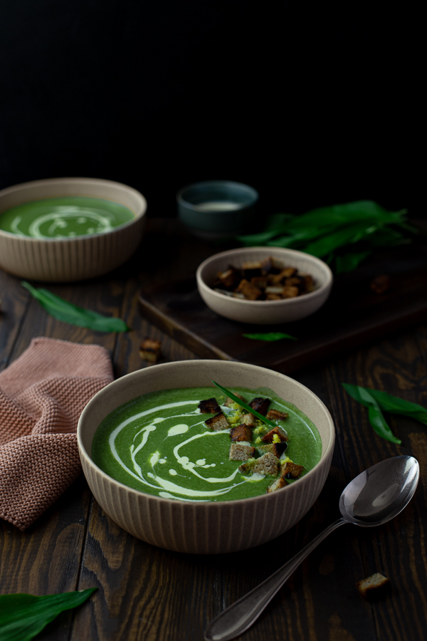 A bowl of bright green vegan coconut wild garlic soup garnished with cream and croutons