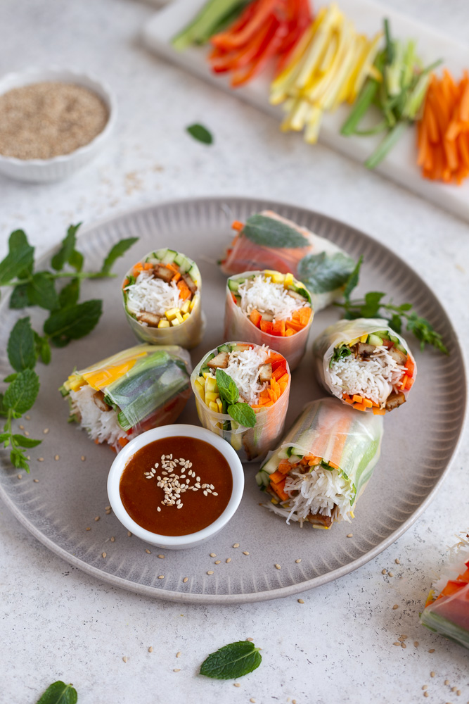 Vegan rice paper rolls next to a bowl with peanut dipping sauce