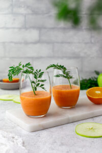 Two glasses of carrot apple smoothie garnished with carrot tops