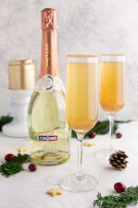 Two glasses of apple cider mimosas in Champagne glasses next to a bottle of Prosecco